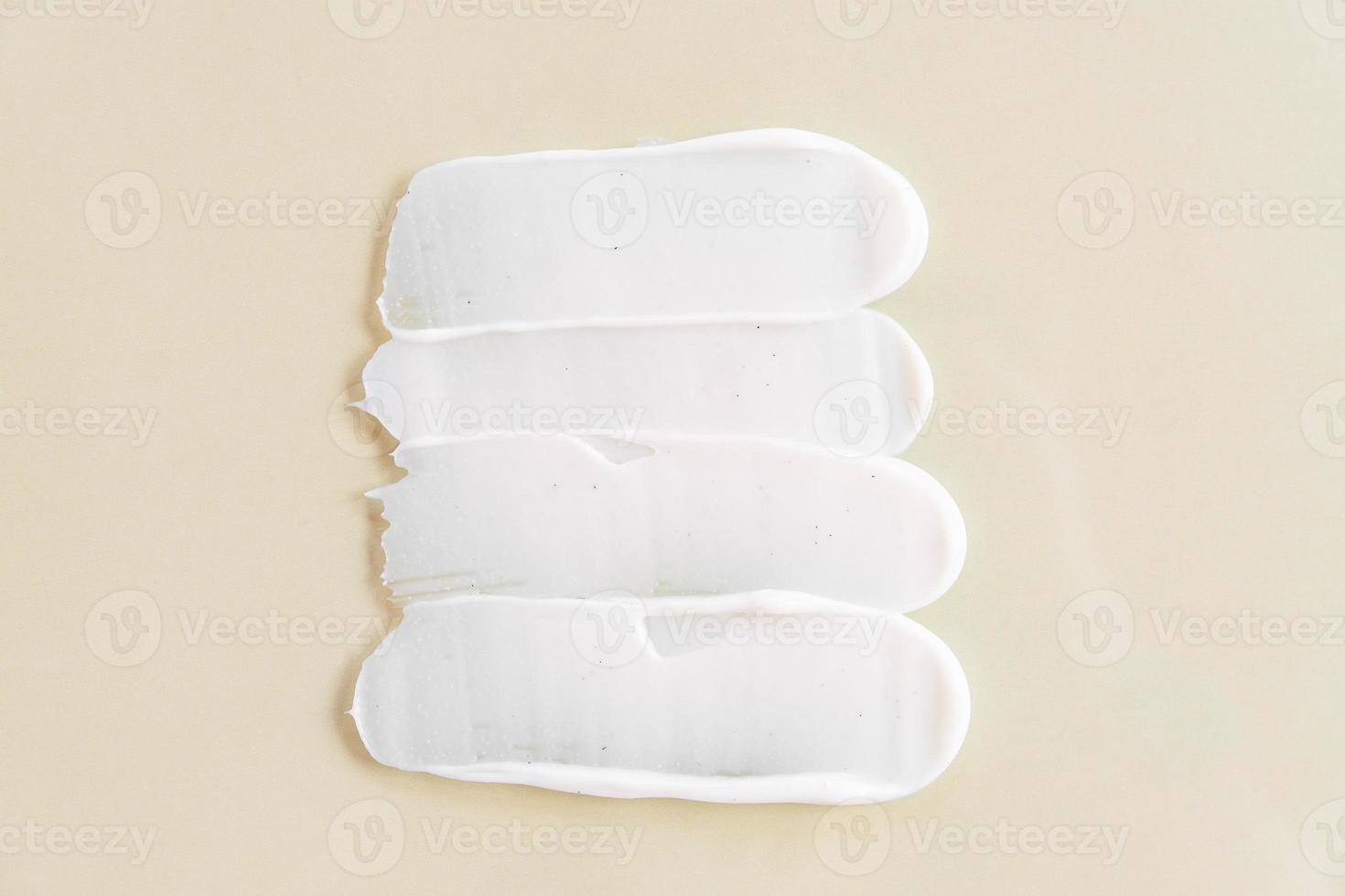 Face cream scrub texture background. exfoliating skincare product smear smudge swatch. Gentle creamy scrub cleanser strokes closeup on beige background photo