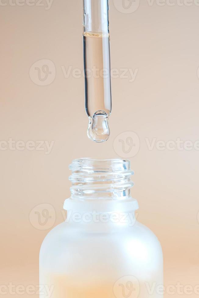 glass cosmetic bottle with a dropper on a beige background with natural essential oil or beauty serum. Natural cosmetics concept, natural essential oil and skin care products photo