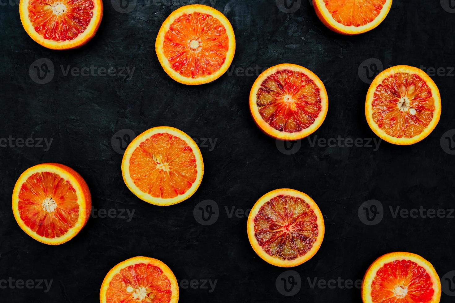 Blood Oranges. Halved blood oranges scattered on a black stone background. Top view, blank space. photo