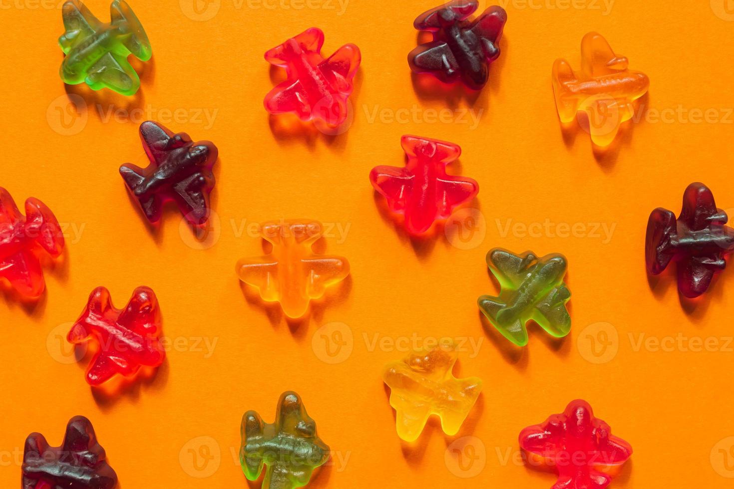 Jelly sweets, colorful marmalade airplanes on oarange background. Open pattern photo