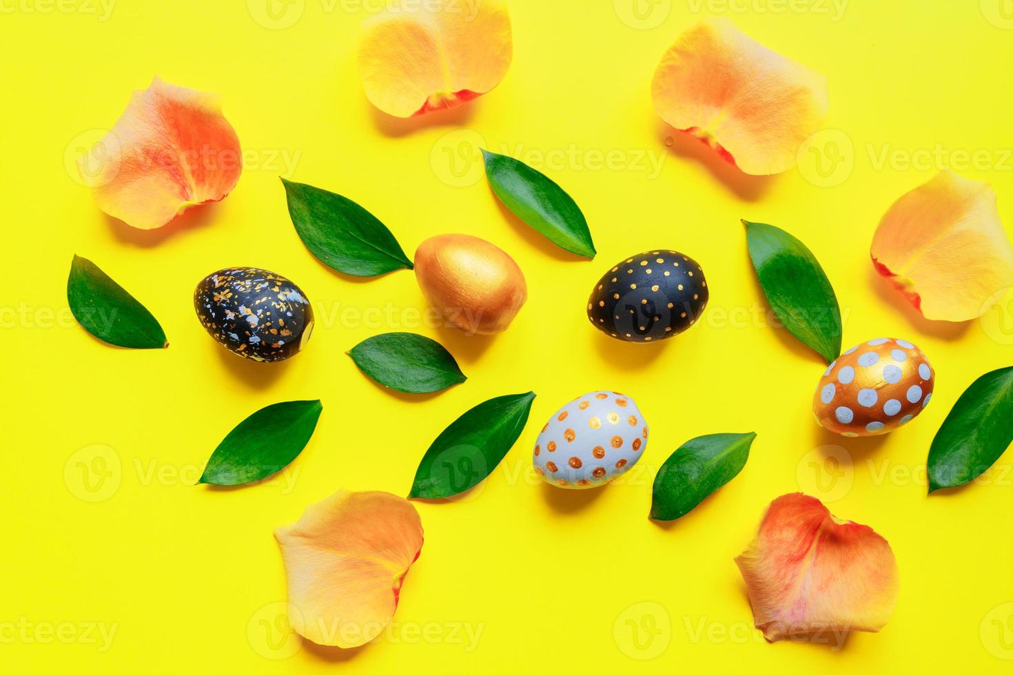 Festive easter background. Golden, black and white stylish pinted eggs with leaves and rose petals on yellow background. photo