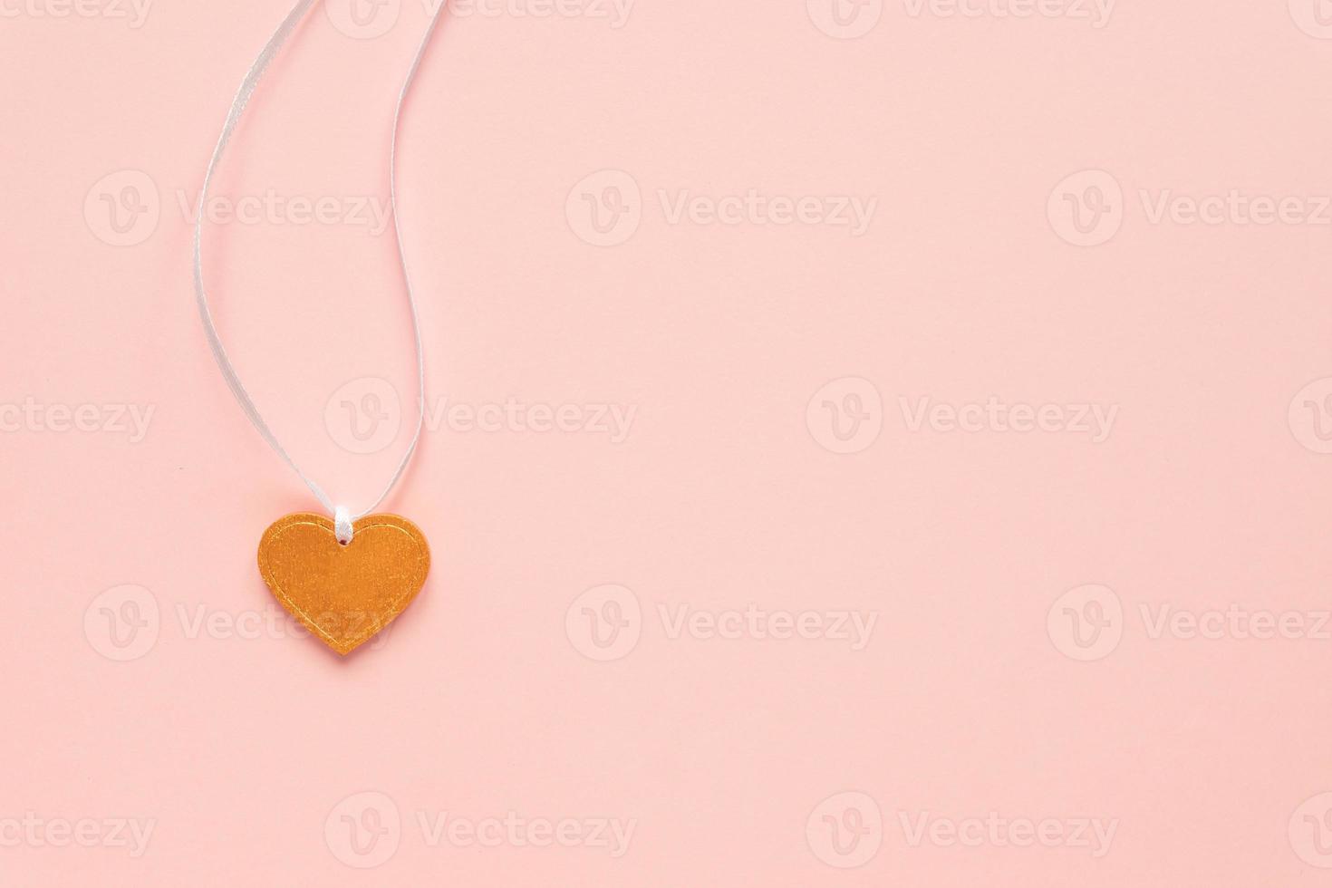 Heart shape golden pendnant on a white ribbon on pink background. Festive Valentine's concept with copy space. Top view photo