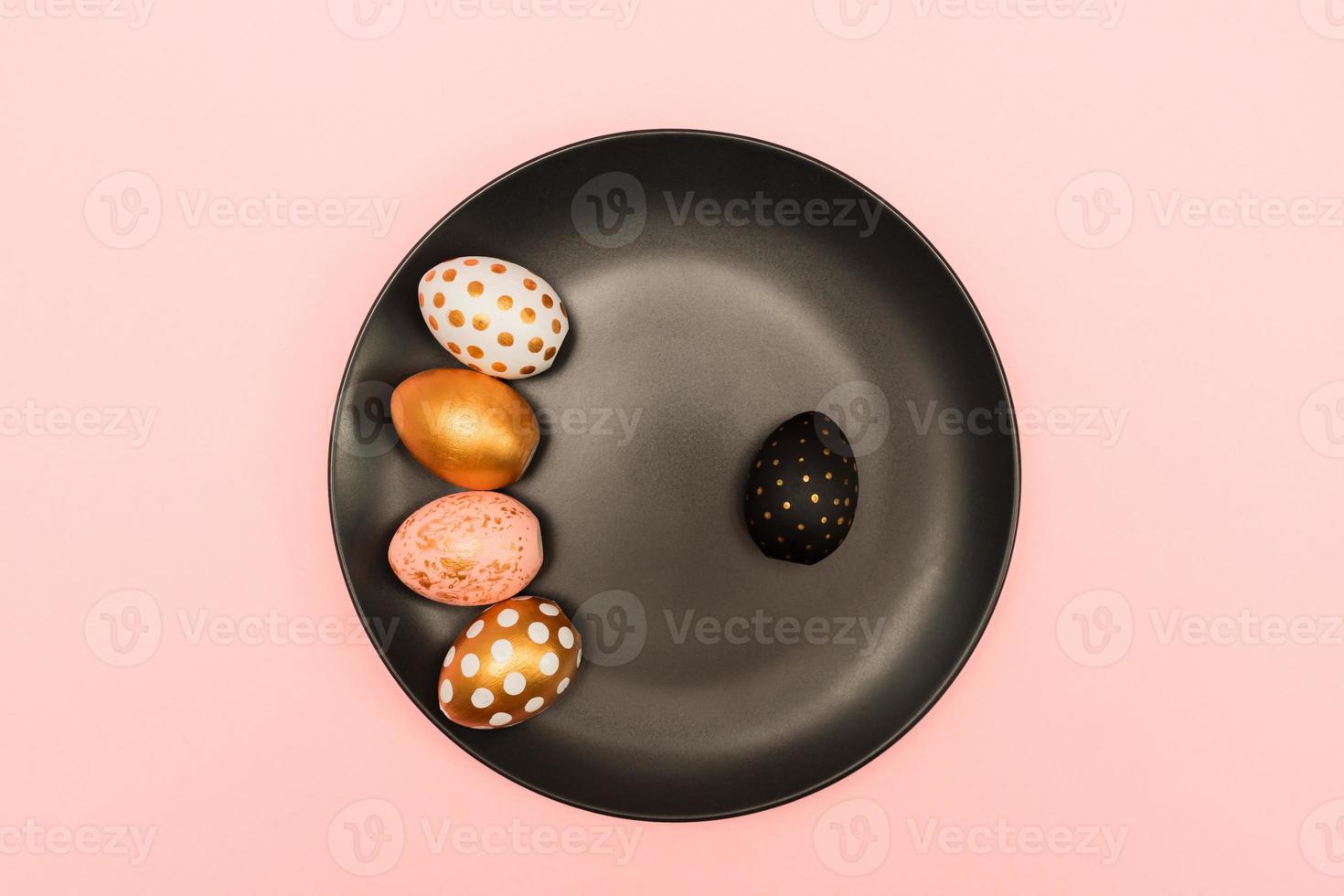 Top view of pink, white and golden decorated eeaster eggs on black plate on pink background. Trendy holiday backdrop photo