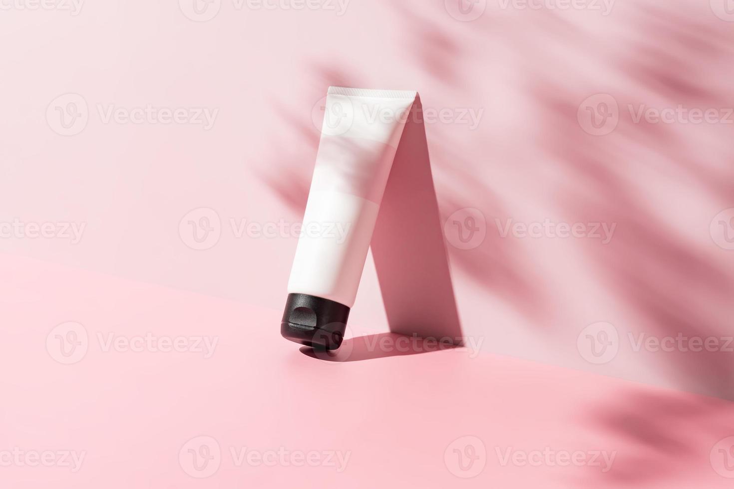 white cosmetic tube for face or body cream, cleanser or shampoo on a pink background with leaves shadows. Concept of minimalism in cosmetic packaging. Copy space photo