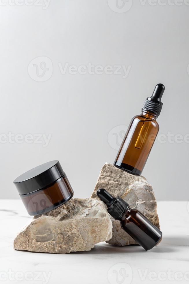 Set natural beauty cosmetic skincare products in glass bottles on stone pedestal, balancing rock pile on gray background. Trendy packaging presentation. photo