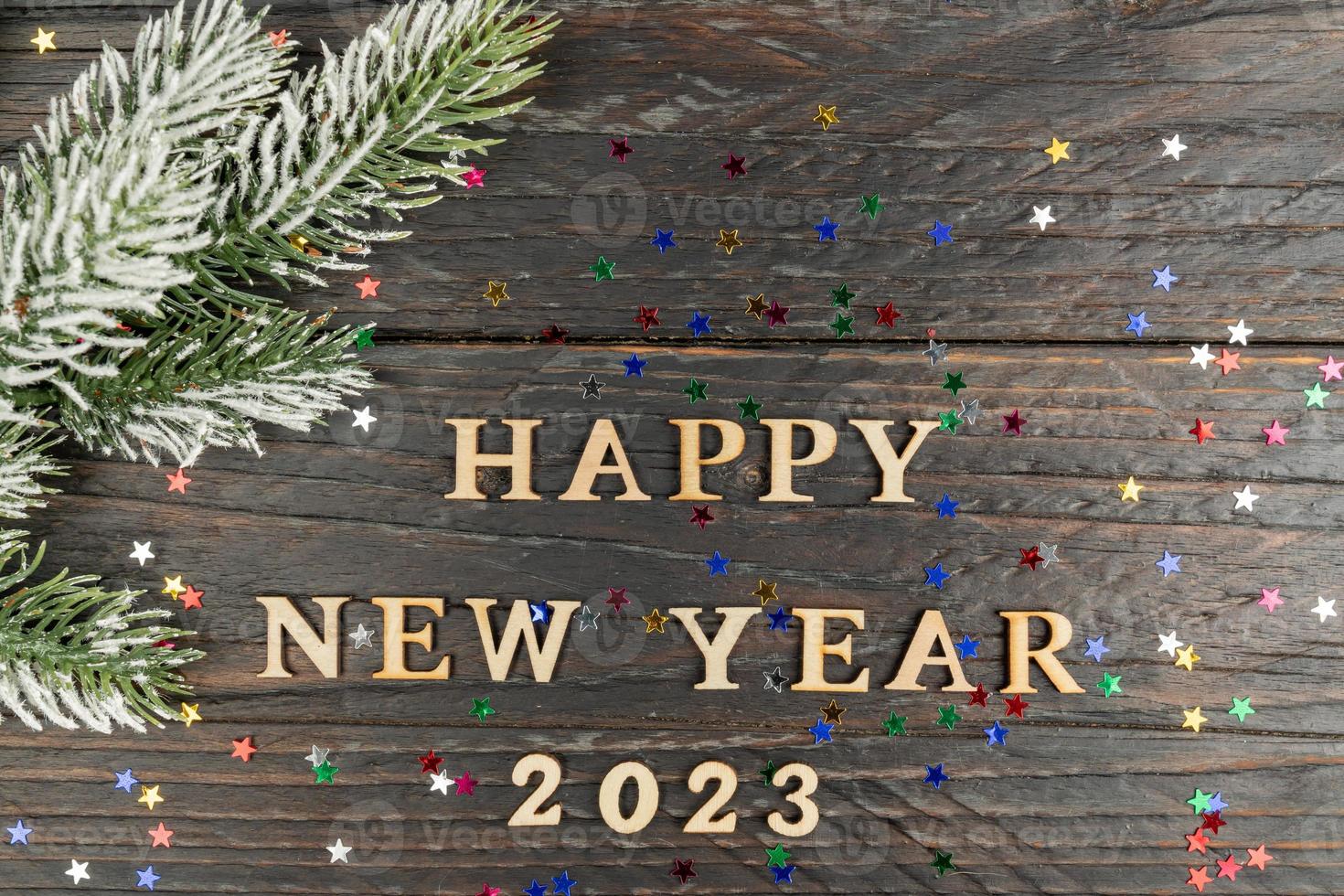 New Year's concept. Happy new year 2023 wooden text on a wooden background, fur-tree branch on the edge of the frame. photo