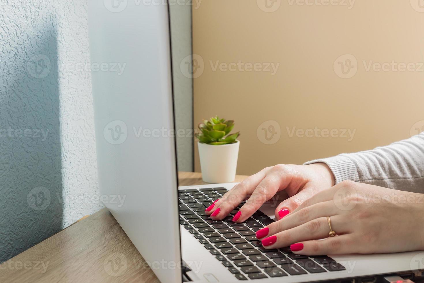 Home office. Open laptop on the table. Caucasian woman with red manicure taping on notebook. photo