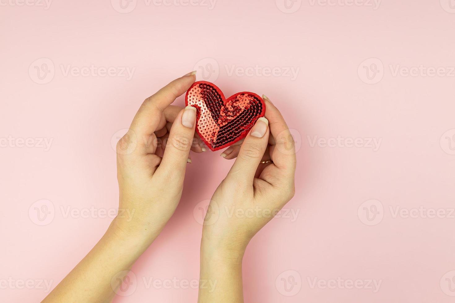 Female hands holding red sequin heart on pink background. Creative minimal layout with copy space photo