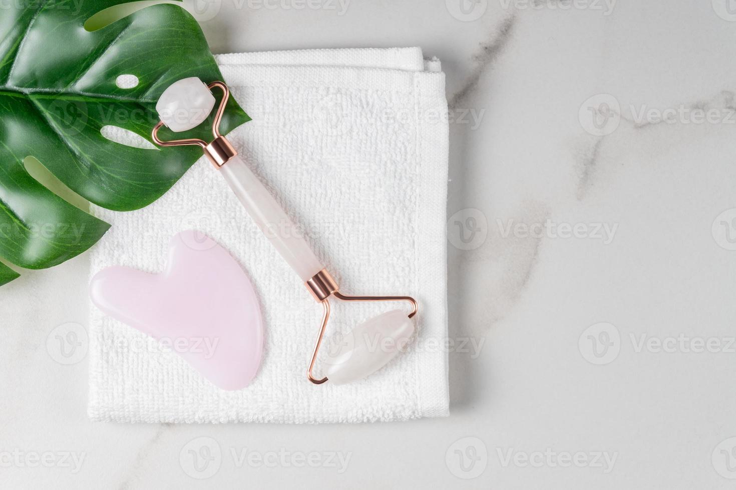 Face rollers, massager guasha scraper, made of natural quartz stone. Self-care set. homemade Spa products on a wtite towel on marble background, the concept of Spa and Wellness with space for text photo