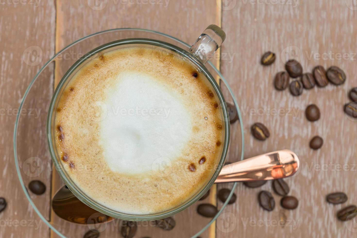 Top view of cup of hot latte or cappuccino in a glass cup on wooden table. Coffee with milk foam with copy space photo