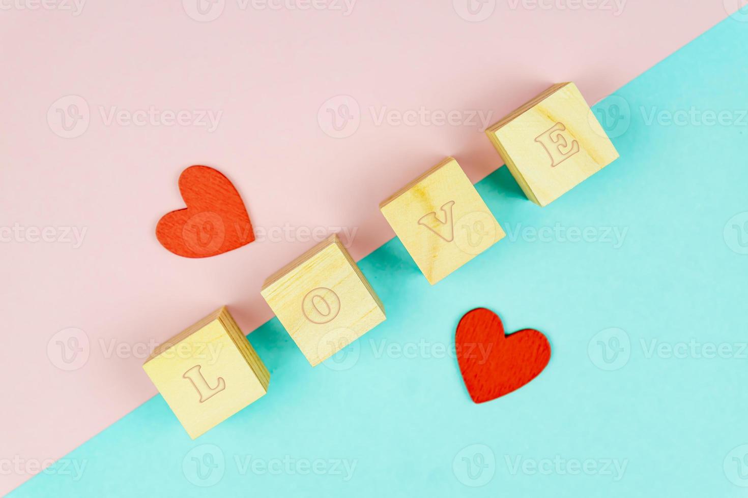 Red hearts and wooden cubes on pink and blue background. Creative flat lay with copy space. Festive greeting card for St Valentines day. Mockup photo