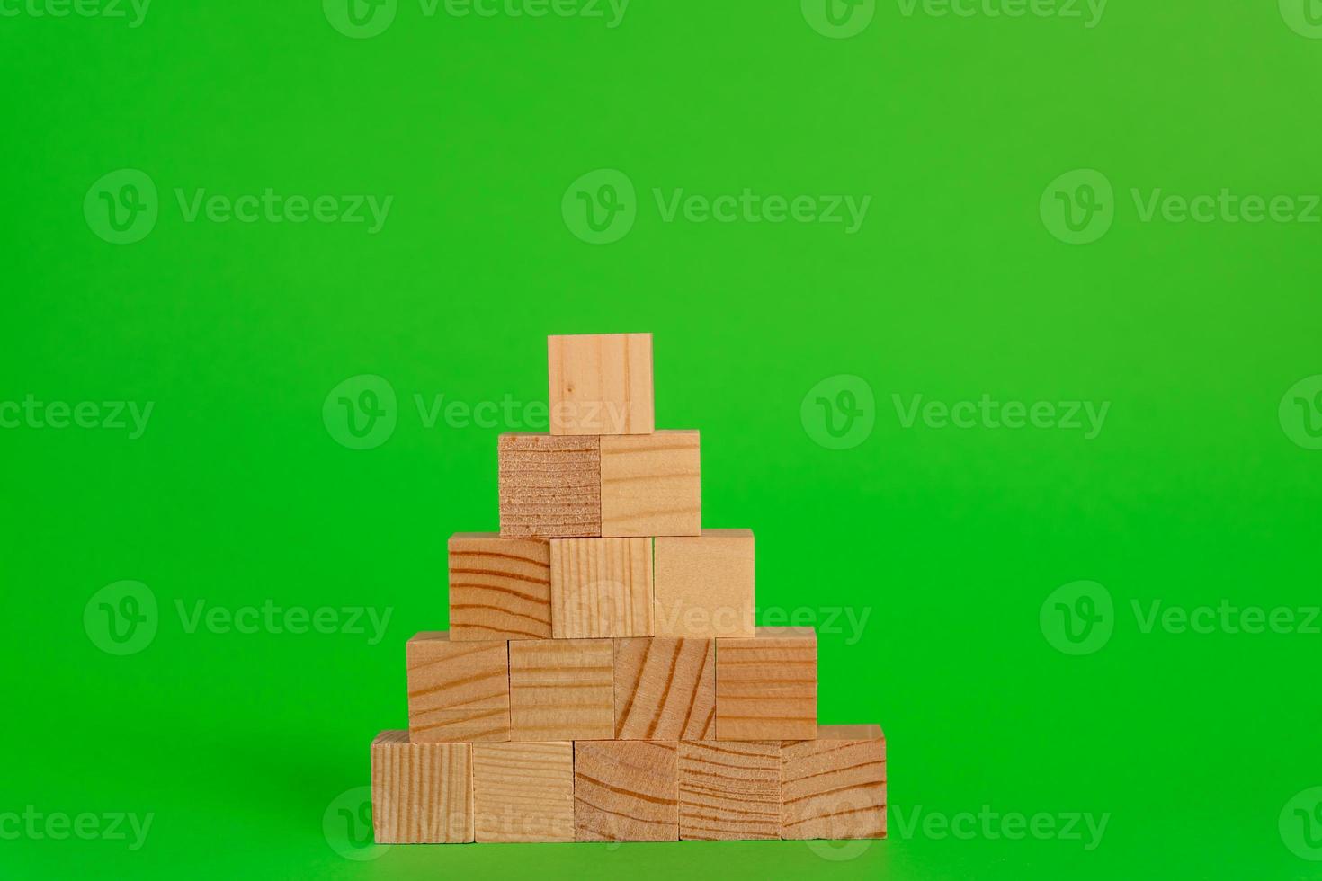 Pyremid Construction made of wooden cubes on green background with copy space. Mockup composition for design photo