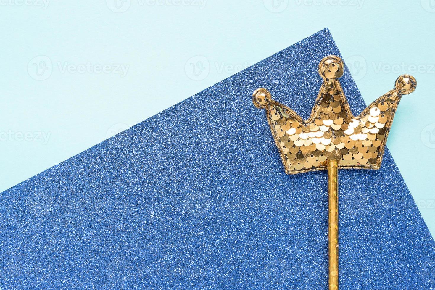 golden magic stick from sequins in crown shape on blue glitter background. Creative flat layclose up photo