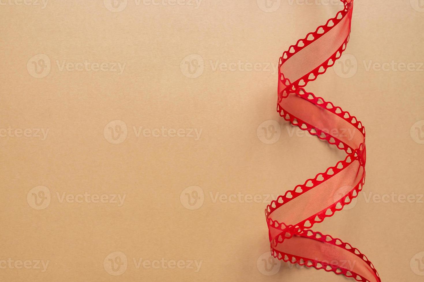 Decorative red ribbon with hearts, twisted in a spiral on a beige background. Fetstive concept with copy space photo