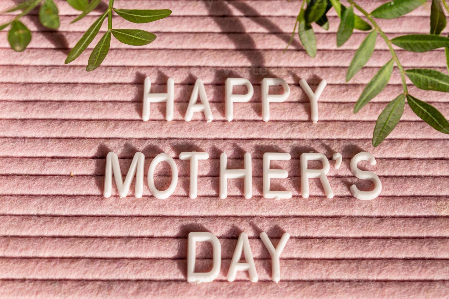 Pink letterboard with quote Happy Mother's Day, decorated with green leaves on pink background. photo