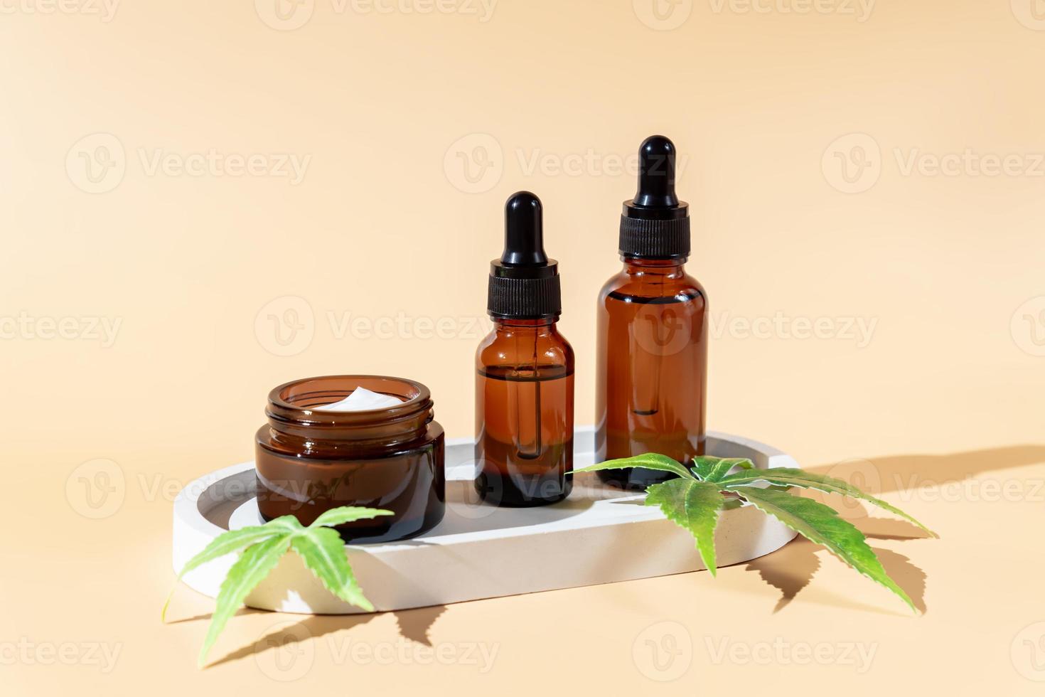 Glass bottles with herbal cbd oil, and face cream or tincture and hemp leaf on pastel beige background. Cosmetics cbd oil. Essential natural oils for face and body. photo