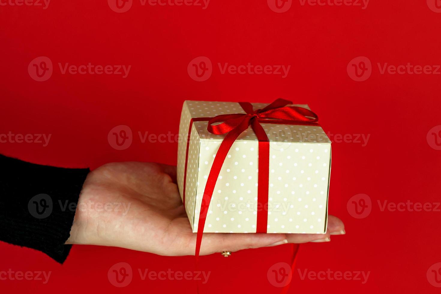 Woman hand holding red present box on red background. Festive creeting card for holidays. photo