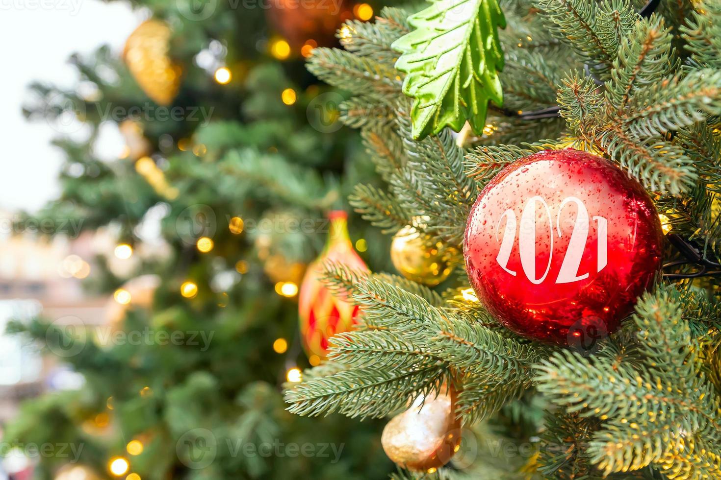 Christmas fir tree decorated with red and golden baubles with 2021 numbers. Bright festive holiday decoration. Blurred background.outdoor ornate banisters. New Year backdrop. photo