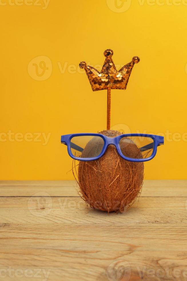 Funny coconut in glasses with sequin crown toned pink. Summer and travel concept photo