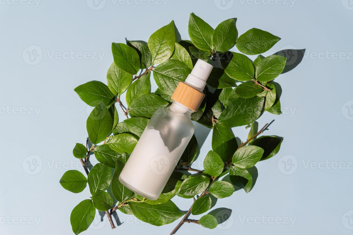 Transparent glass cosmetic bottle with a pusher on a blue background with tropical leaves. Natural cosmetics concept, natural essential oil and skin care products. photo
