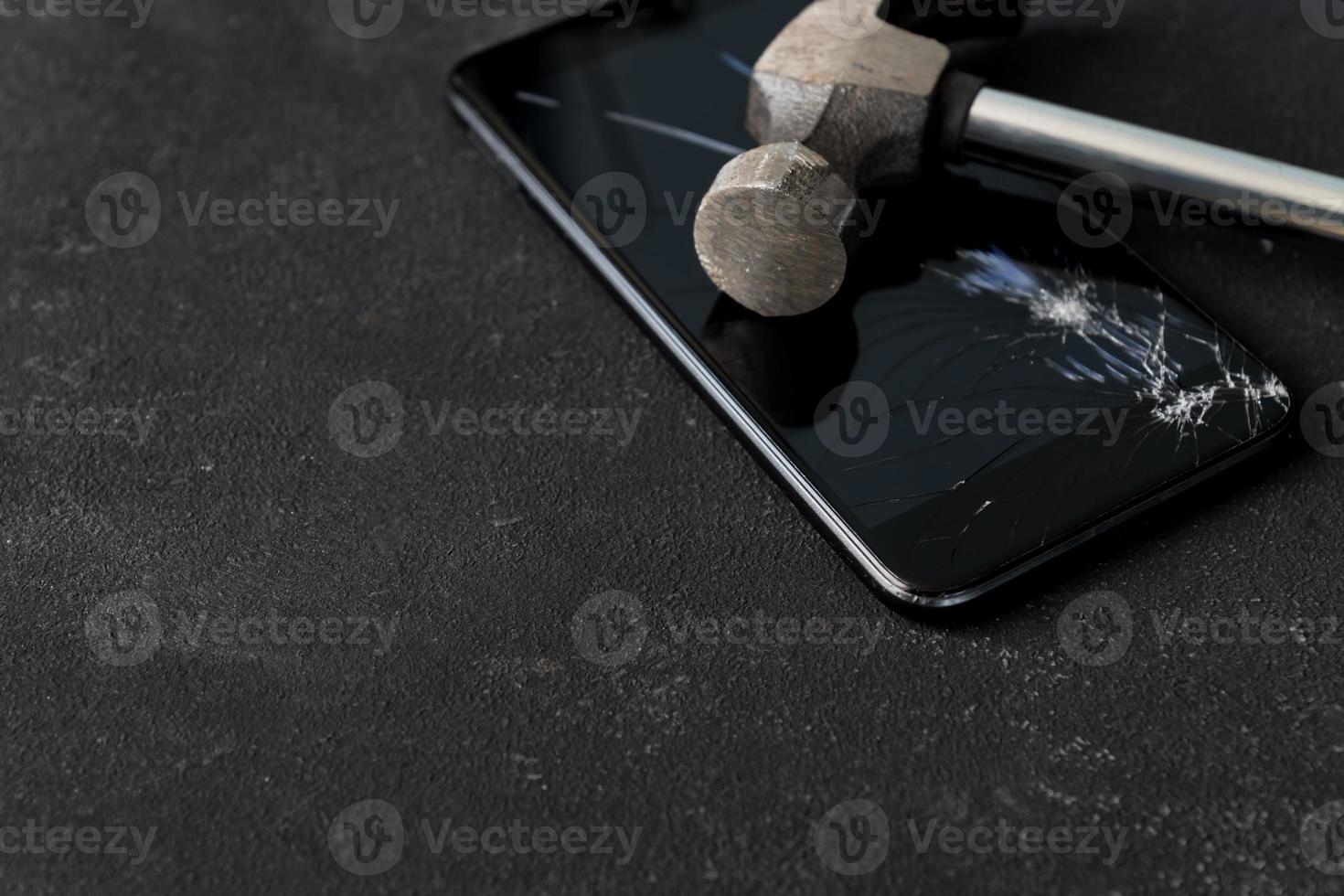 Broken mobile phone screen with a big black iron hammer. LCD screen broken, cracked and unusable smart phone. photo