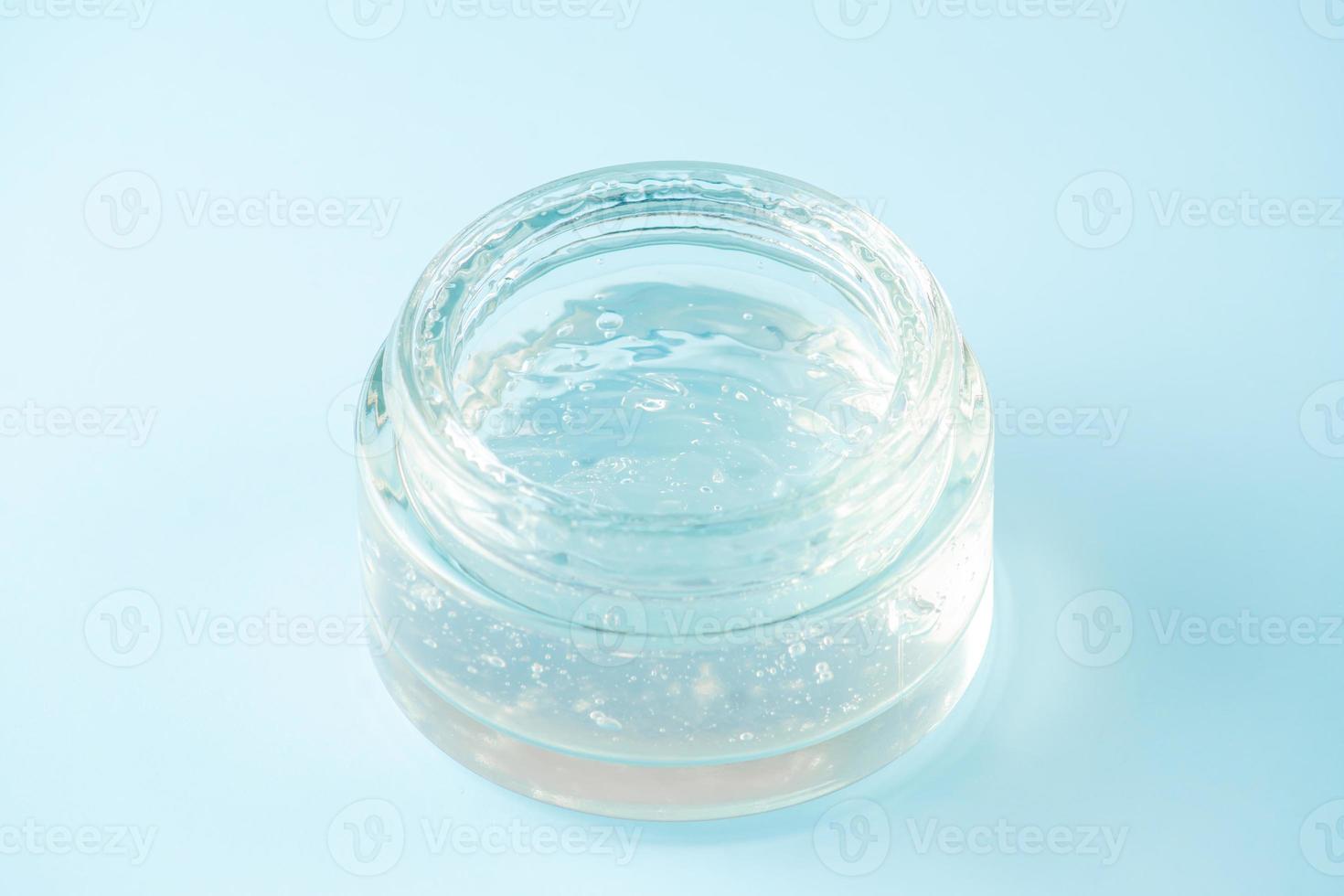 Transparent gel jar on blue background. Cosmetic gel with bubbles texture close up. Clear colored liquid beauty product sample photo