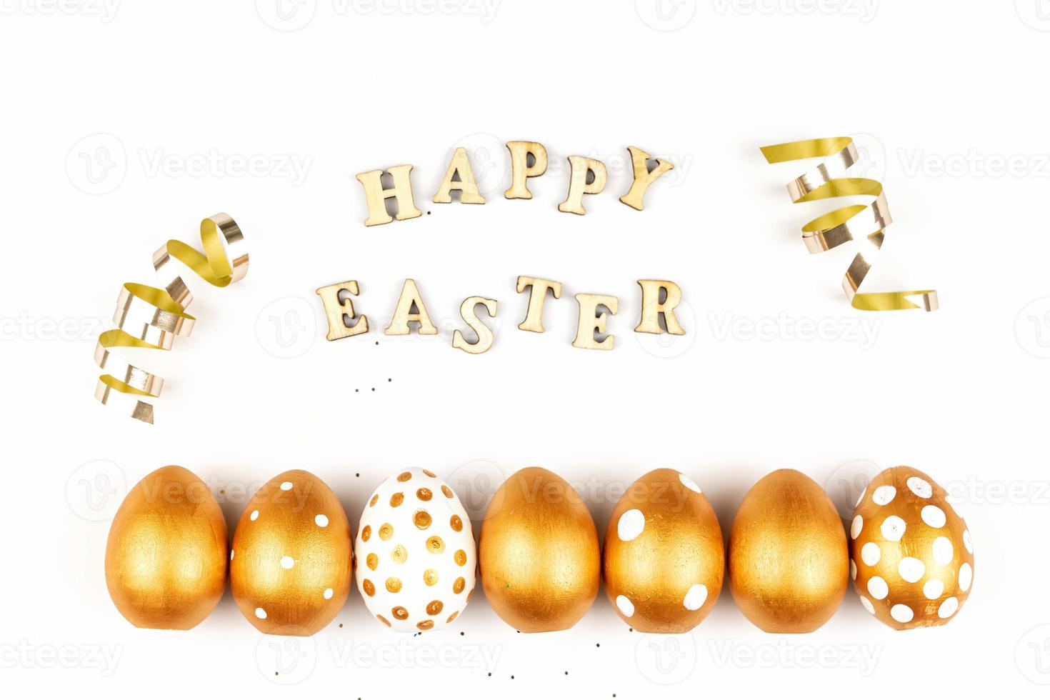 Easter festive decoration. Top view of easter eggs colored with golden paint and inscription in English Happy Easter. Wooden letters on white background. Various dotted design photo