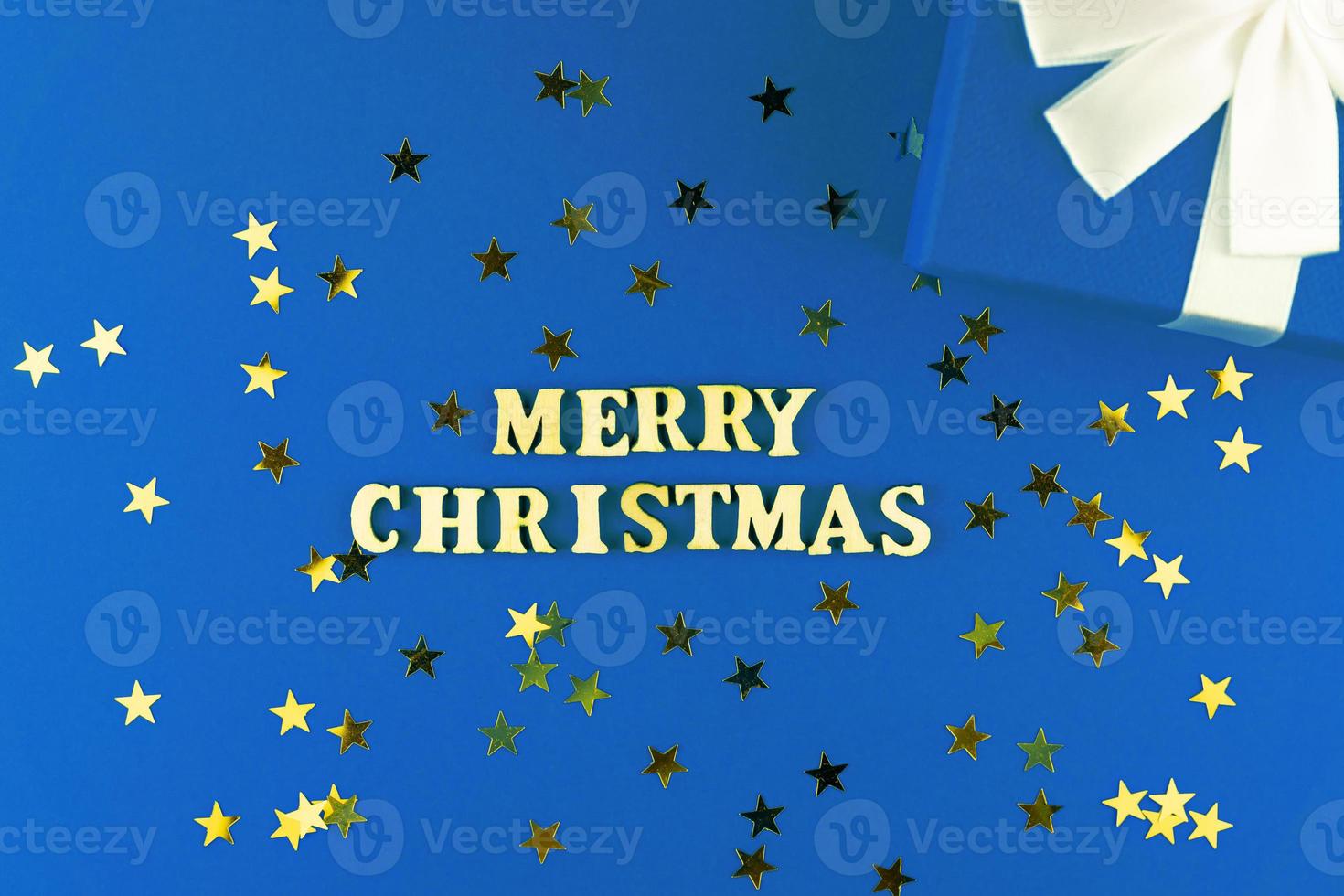 wooden letters on blue background. Merry christmas lettering on blue paper with scattered stars confetti and gift box. photo