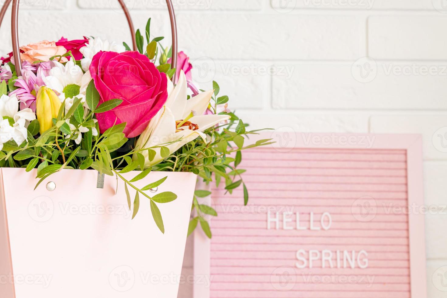 Hello Spring - text on pink felt letter board with blooming flowers and green leaves on whitebrick wall background. Springtime concept. Interior design photo