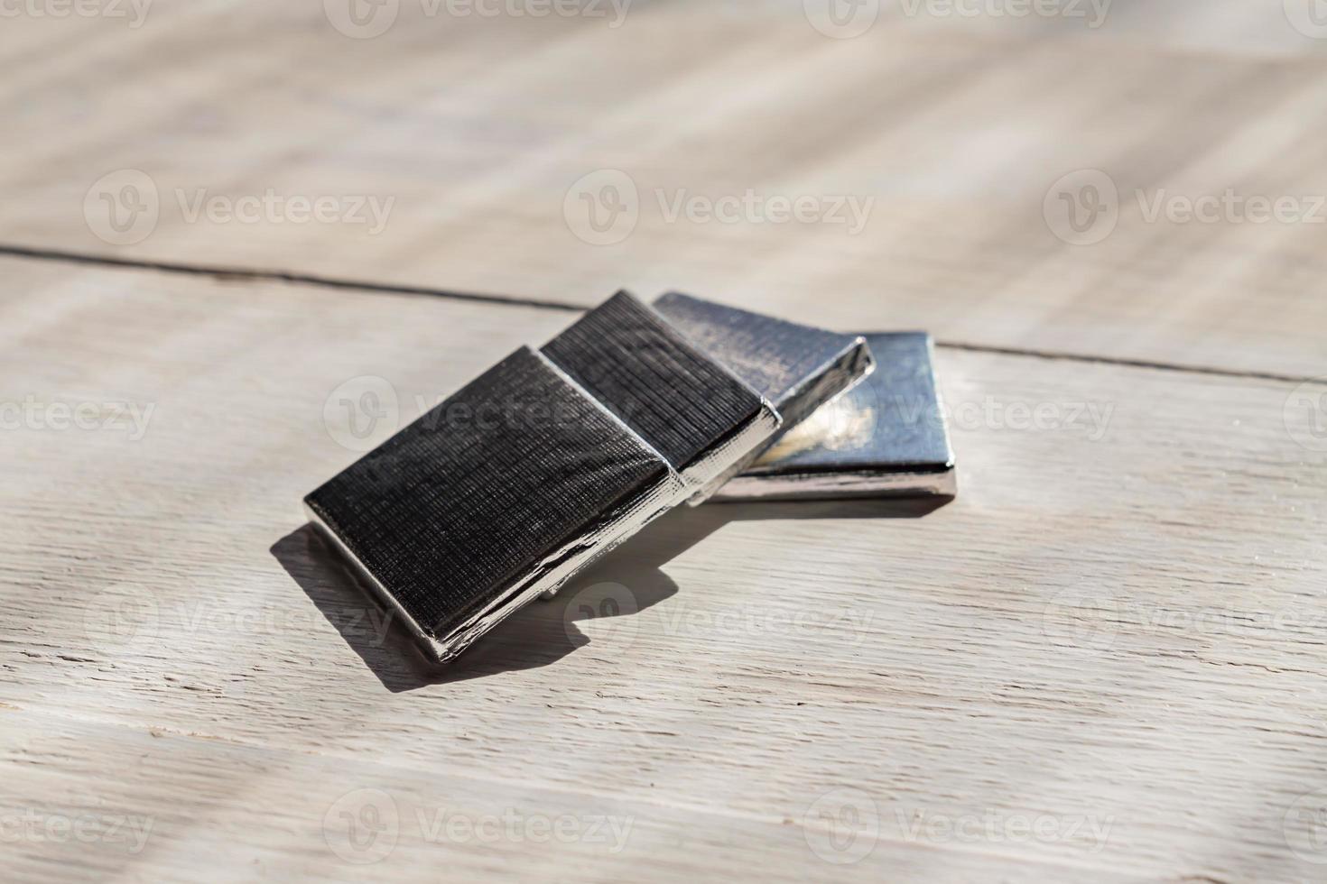 Mini chocolate bars in silver paper on white wooden background. Natural cocoa product in portion package. photo