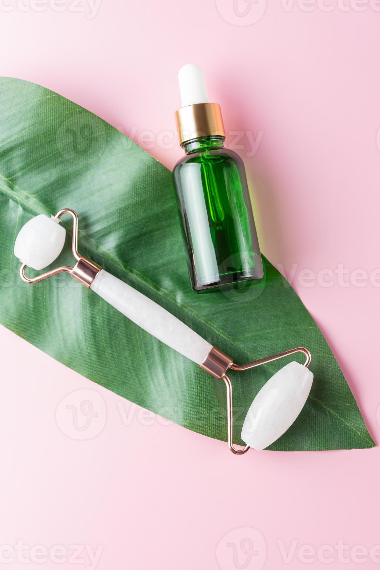 Quartz stone face roller, gua sha and massage lotion on pink background