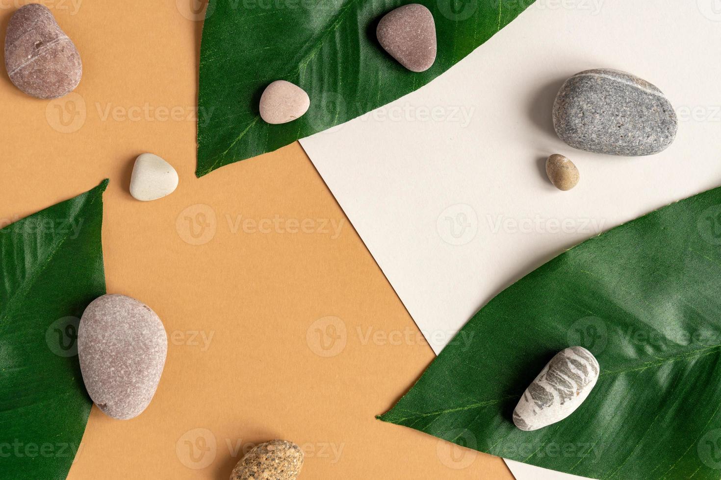 Zen flat lay composition with green leafs and stones. Tropical leaf and sea pebble on beige background. Spa or beauty template with place for text or product . Blank card with tropical leaves. photo