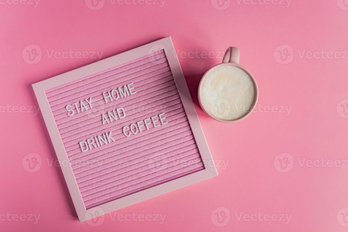 Top view of Pink Coffee cup with cappuccino and qoute Stay home and drink coffee. Self isolation and quarantine campaign to protect yourself from pandemia photo