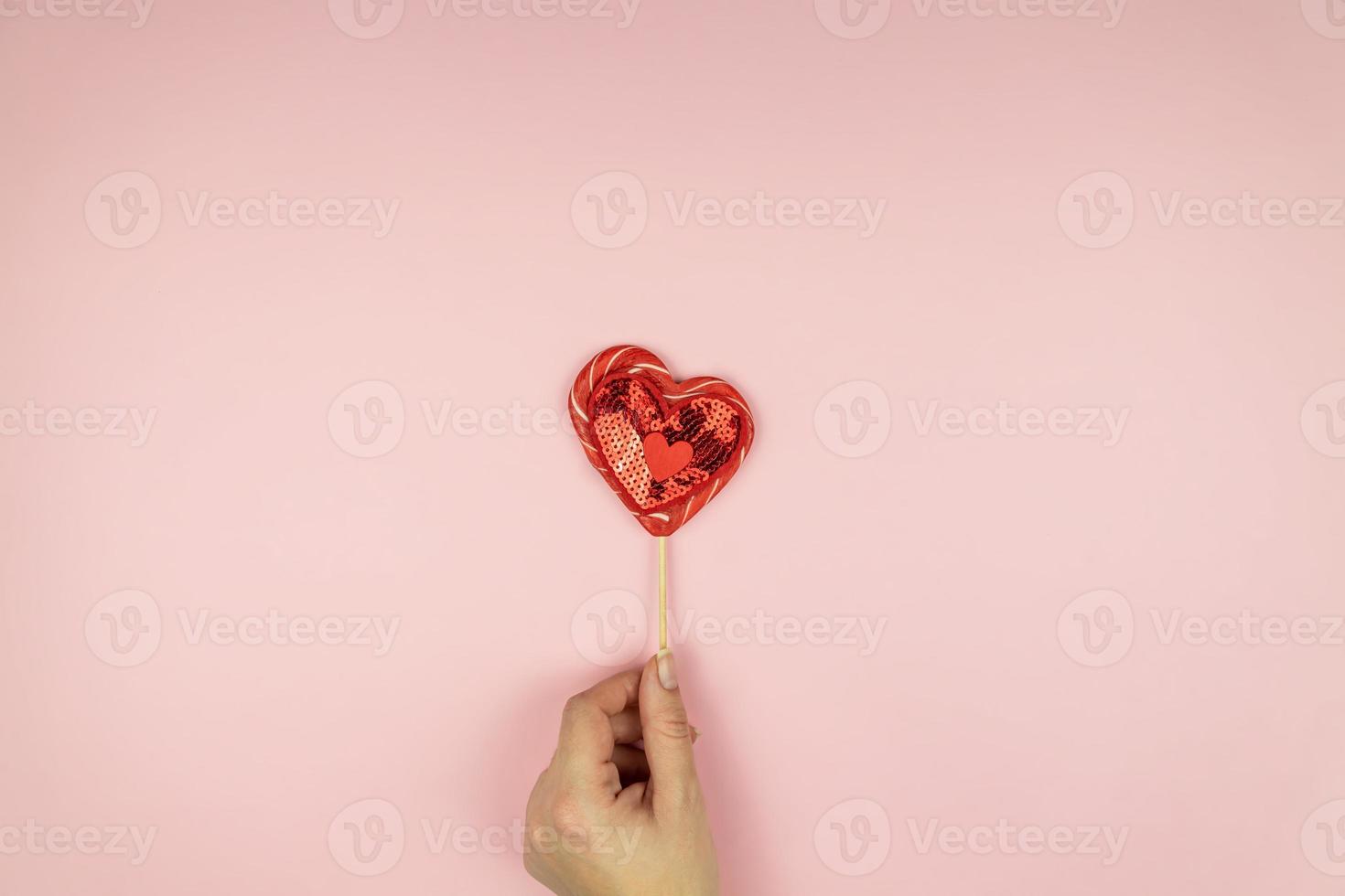 Female hands holding red sequin heart on pink background. Creative minimal layout with copy space photo