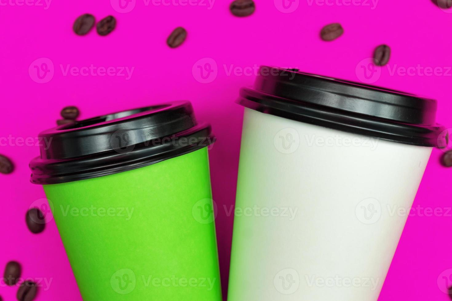 Top view of paper dispocable coffee cups on pink background with coffee beans. photo