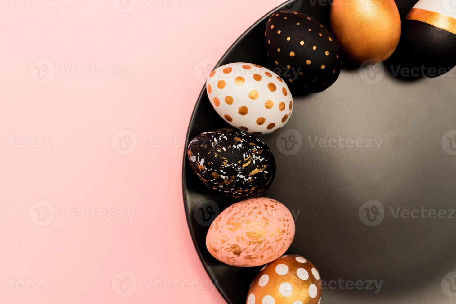Top view of pink, white and golden decorated eeaster eggs on black plate on pink background. Trendy holiday backdrop photo