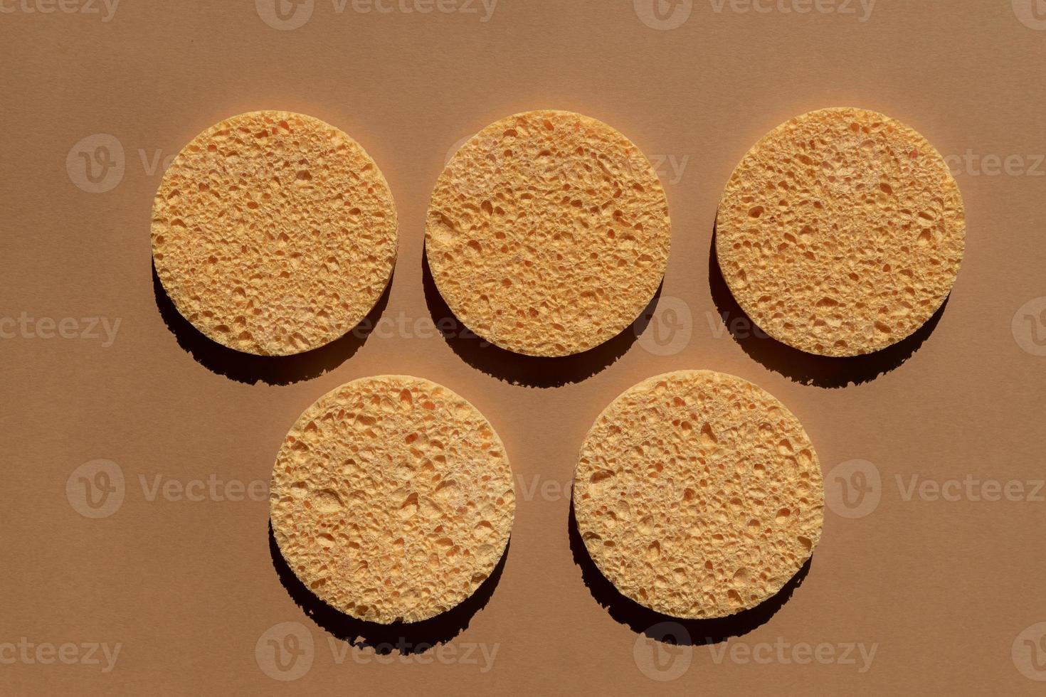 conjunto de esponjas de celulosa redondas naturales para limpieza facial y eliminación de maquillaje sobre fondo marrón foto
