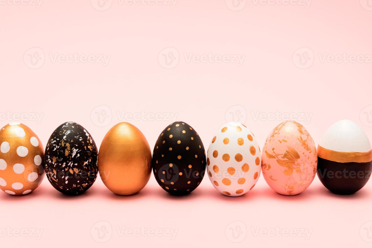 Side view of pink, white, black and golden decorated easter eggs in a row on pink background. Trendy holiday backdrop. photo