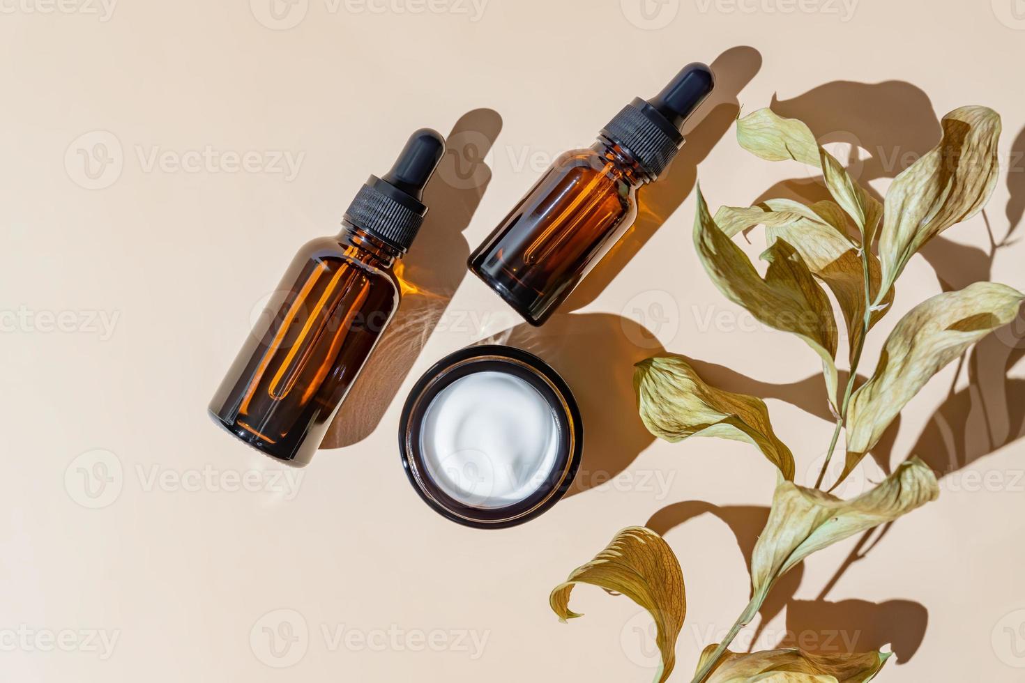 Face and eye moisturizer cream and serum in a glass bottles and jar and dried herb on light beige background. Concept eco organic natural cosmetic products for skincare. photo