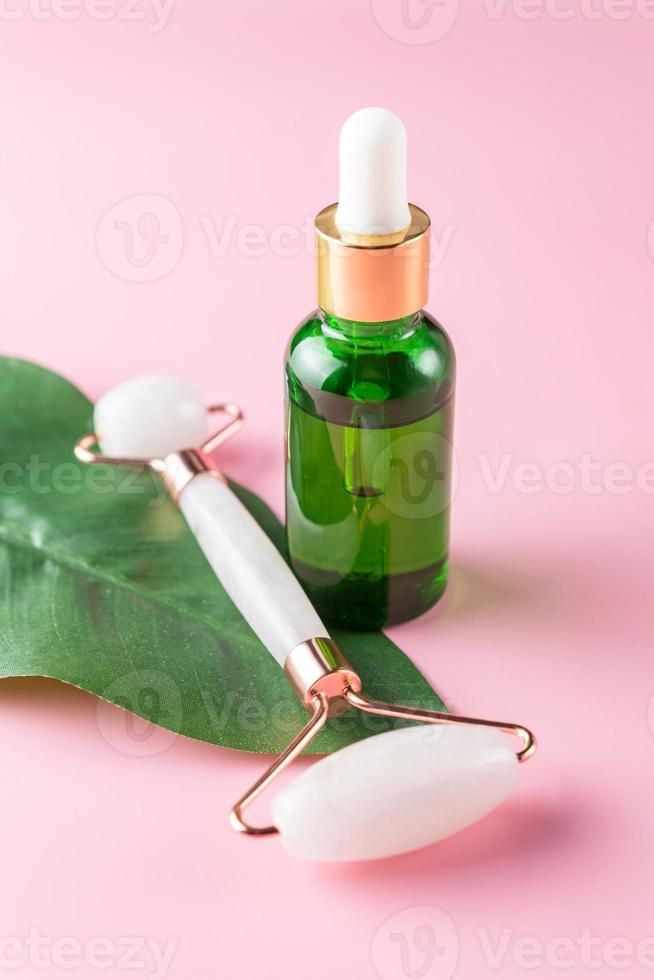 Natural face oi in green pipette bottle and quartz massaging roller with green leaf. Home spa procedures presentation. Unbranded package photo