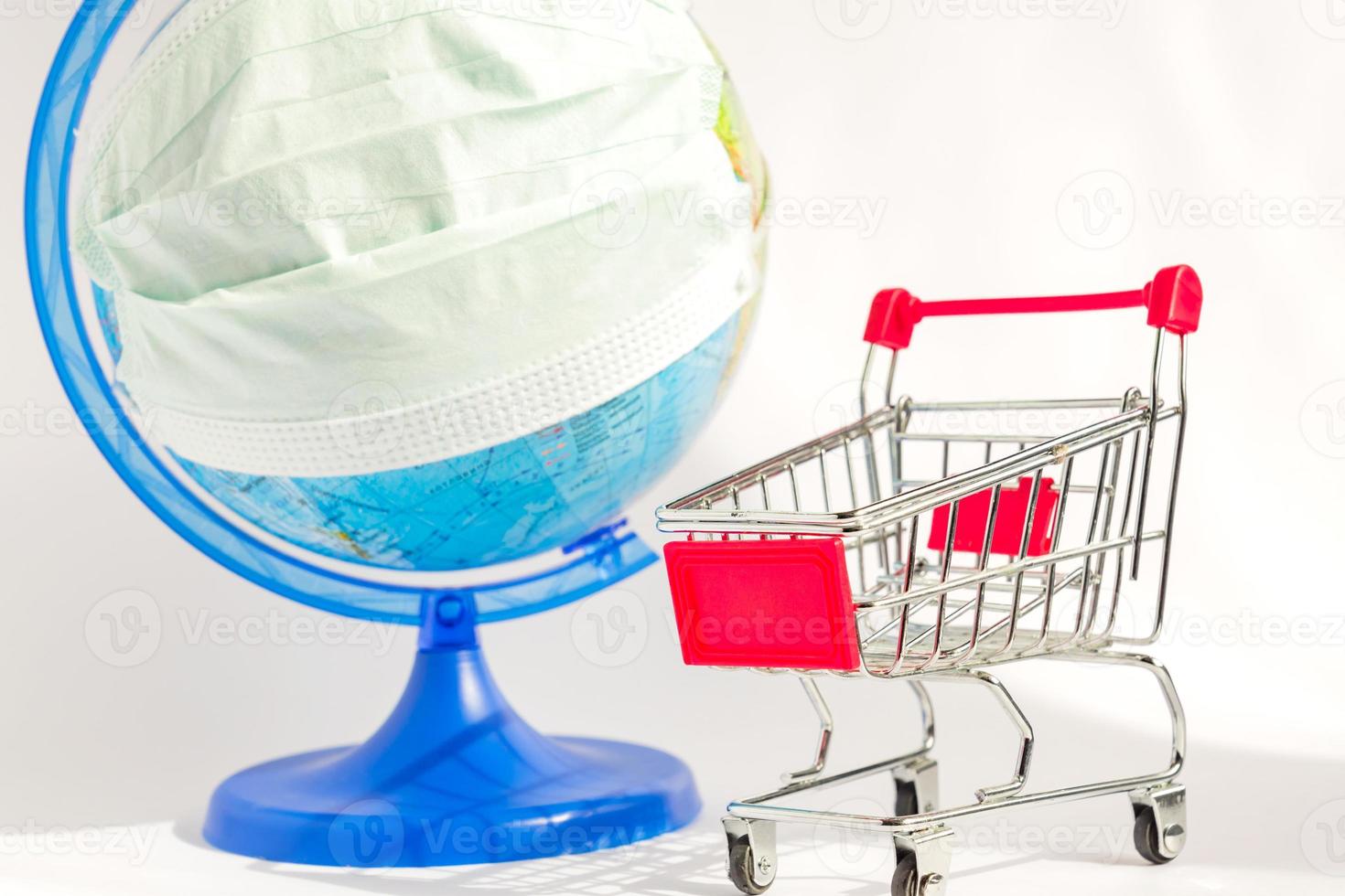 Coronavirus outbreak. World pandemia. Globe in medicine mask and shopping trolley on white background. Concept of online shopping during covid-19. photo