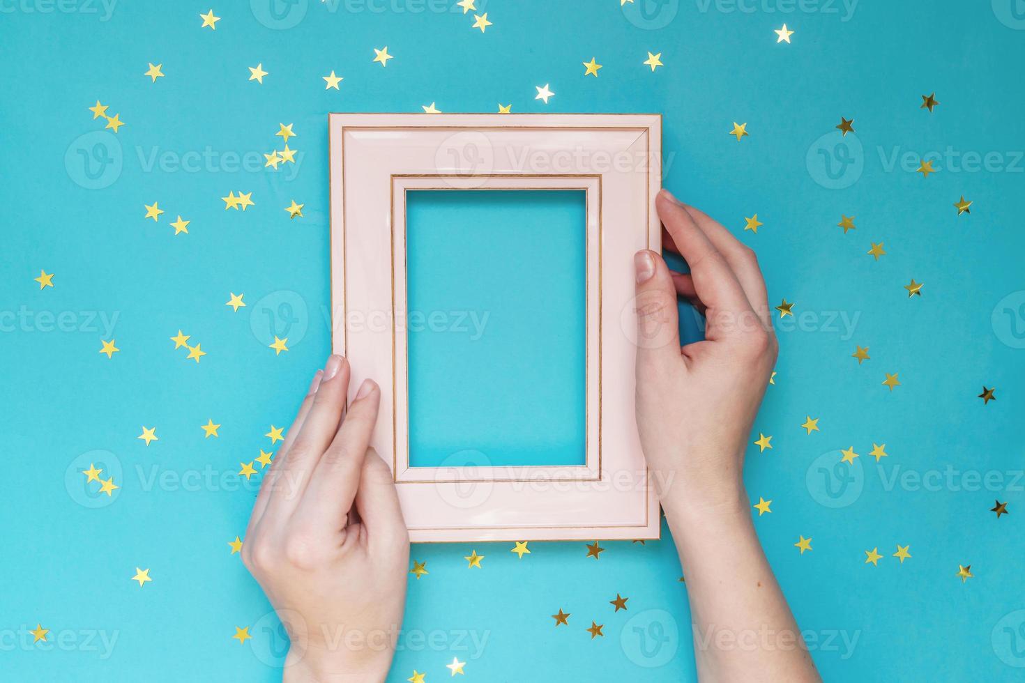 femal hand holding pink foto frame on blue background with scattered gold stars. Creative Mockup. photo