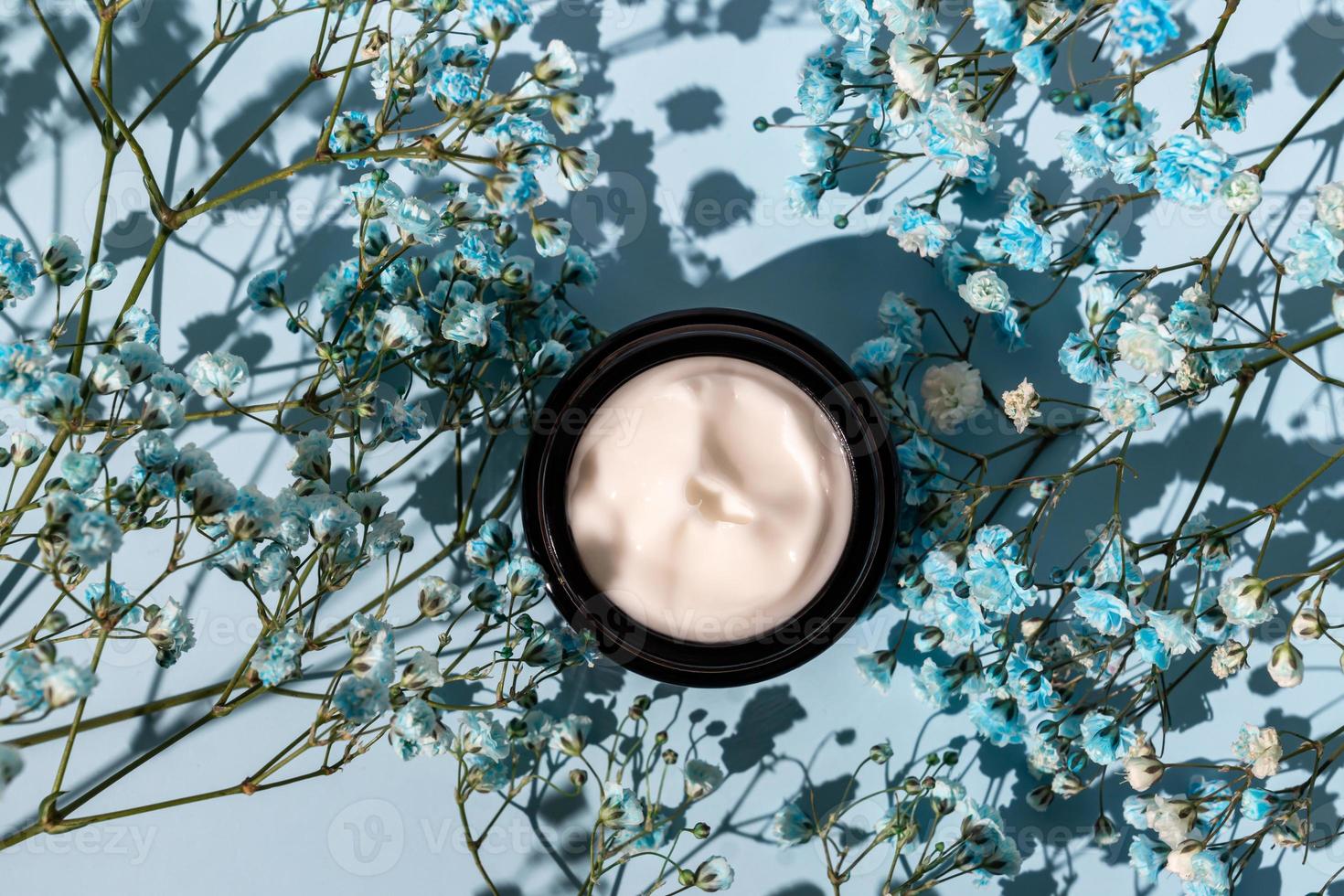 anti-aging collagen facial cream in dark glass jar with bloomon flowers of gypsophila on blue background. Natural Organic Cosmetic Beauty Concept. photo