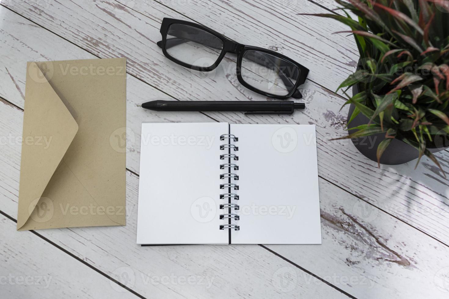 Notepad with brown envelop, reading glasses, pen and potted plant on wooden desk photo