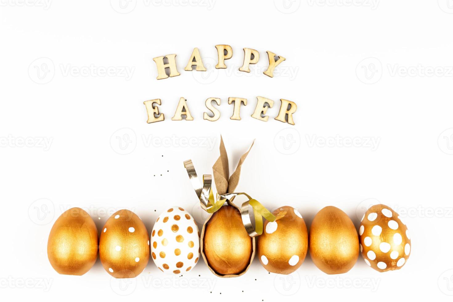 Easter festive decoration. Top view of easter eggs colored with golden paint and inscription in English Happy Easter. Wooden letters on white background. Various dotted design photo