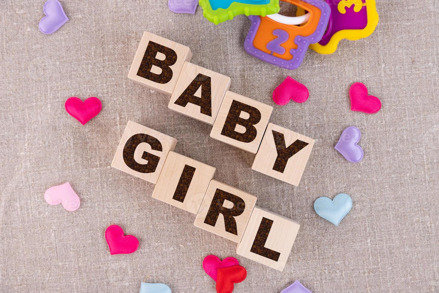 Wooden blocks with the word Baby girl and small colorful hearts underneath. View from above photo