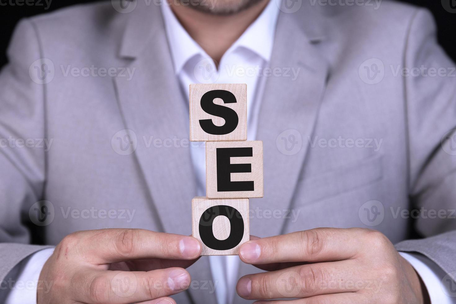 SEO search engine optimization, text is written on wooden cubes against the background of a businessman in a gray jacket sitting at the table. photo