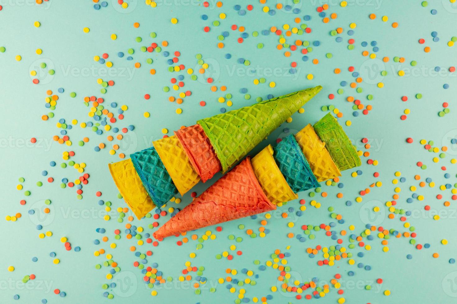Set of various bright multicolored ice-cream waffle cones on blue background with scattered confetti sugar sprinkles. photo