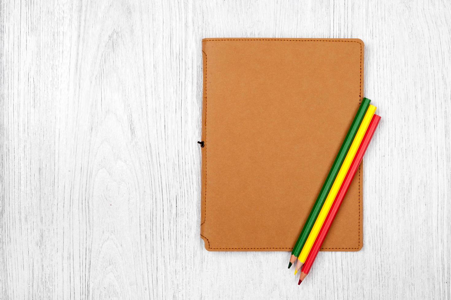 cuaderno marrón y lápices de colores sobre una mesa de madera blanca, vista superior foto