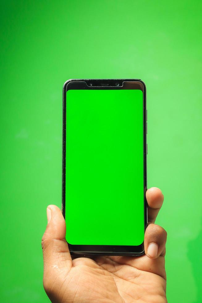 Hand holding smartphone, green screen. photo